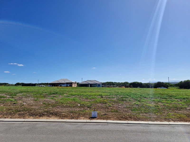 A view of a vacant residential plot from the street, featuring level ground and surrounding neighbourhood development.