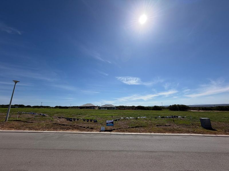 A vacant residential plot of land featuring a paved road frontage, kerbing, and existing utility connections, ready for development.
