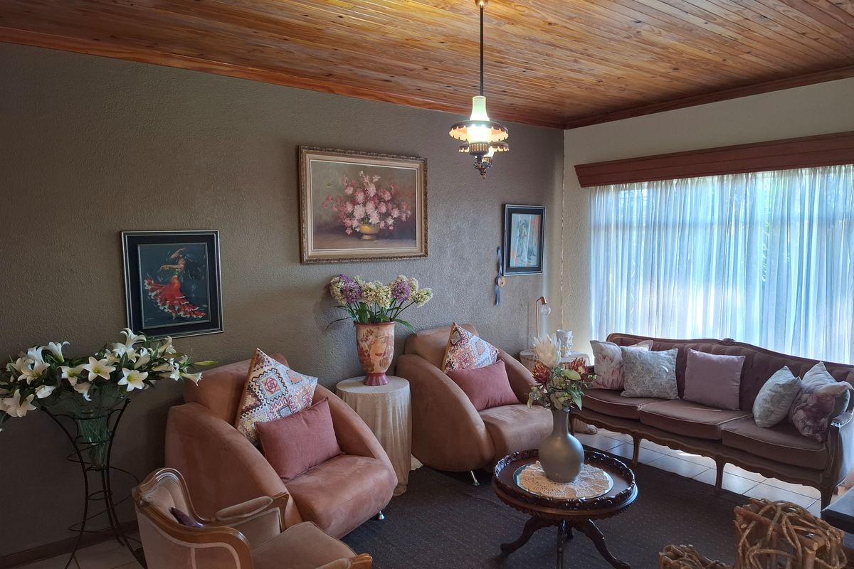 A cozy living room featuring a warm timber tongue and groove ceiling, large window with natural light, and a classic pendant light fixture.