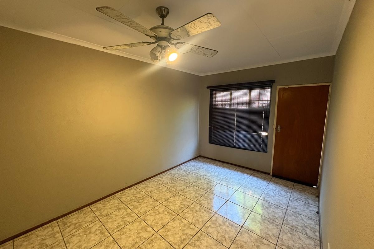 An empty bedroom featuring tiled flooring, a ceiling fan, and a wooden door with venetian blinds.