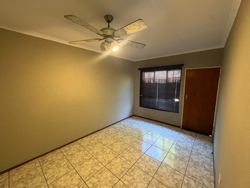 An empty bedroom featuring tiled flooring, a ceiling fan, and a wooden door with venetian blinds.
