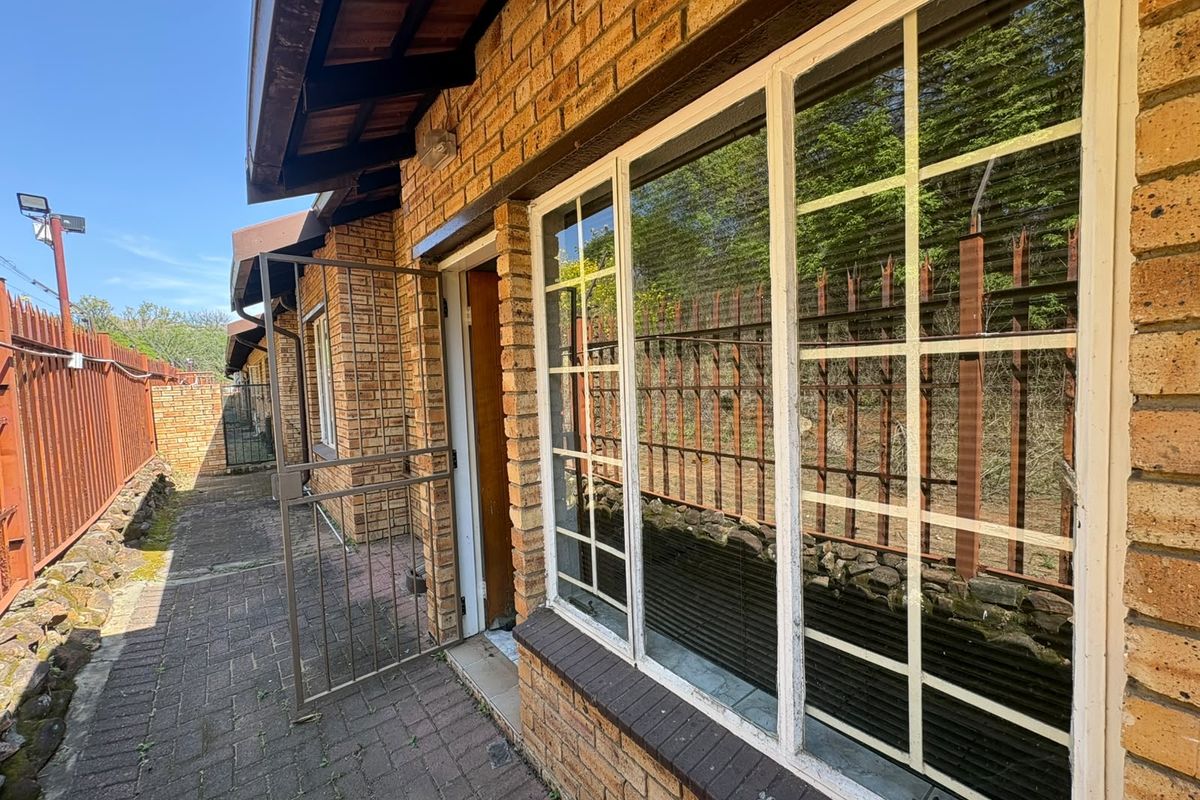 Rear exterior view of the apartment featuring a brick facade, paved walkway, and security-focused metal window frames and perimeter fencing.
