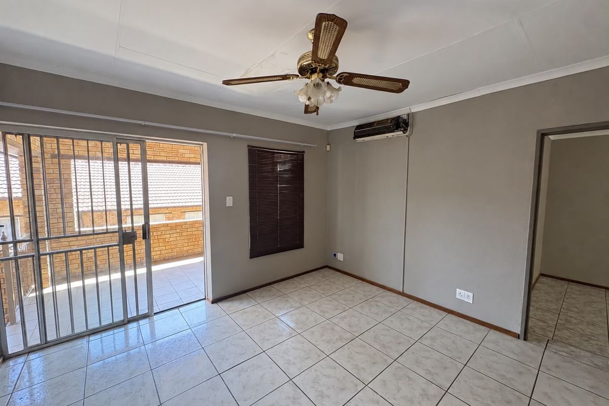 An empty living room featuring tiled floors, a ceiling fan, a wall-mounted air conditioner, and a sliding door leading to an outdoor balcony.