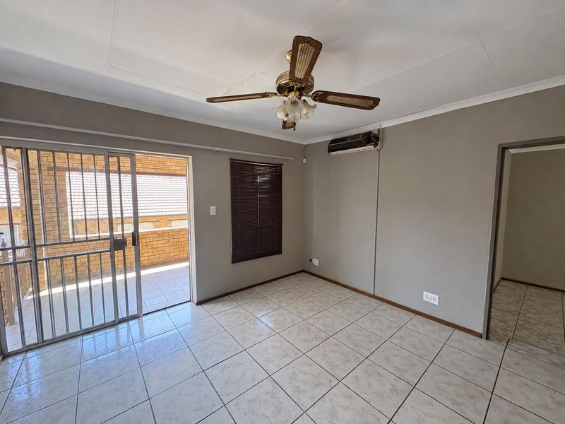 An empty living room featuring tiled floors, a ceiling fan, a wall-mounted air conditioner, and a sliding door leading to an outdoor balcony.