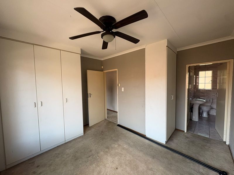 A vacant bedroom featuring built-in cupboards, a ceiling fan, and direct access to an en-suite bathroom.