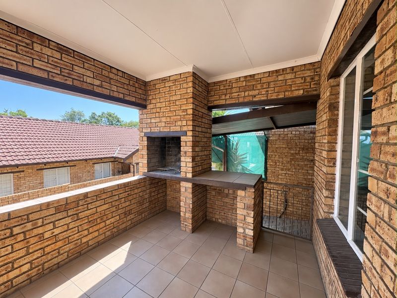 A covered balcony featuring a built-in brick braai and tiled flooring, offering a functional outdoor entertainment space.