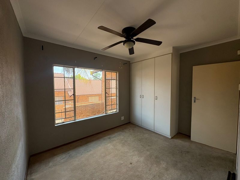 An empty bedroom featuring built-in cupboards, a ceiling fan, and carpeted flooring, offering a blank canvas for personalization.