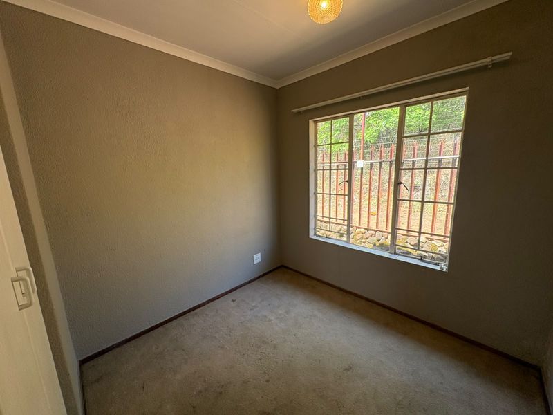 An empty bedroom featuring carpeted flooring, built-in cupboard storage, and security bars on the window.