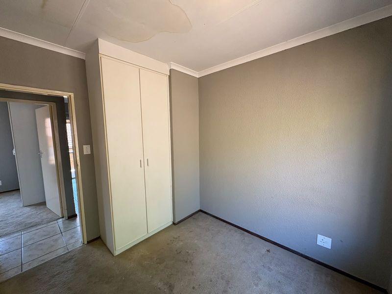 An empty bedroom featuring a built-in wardrobe, neutral wall paint, and carpet flooring, showing signs of ceiling water damage and floor staining.