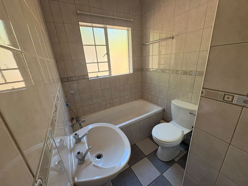 A functional bathroom featuring a bathtub, pedestal basin, and toilet with neutral wall and floor tiling.