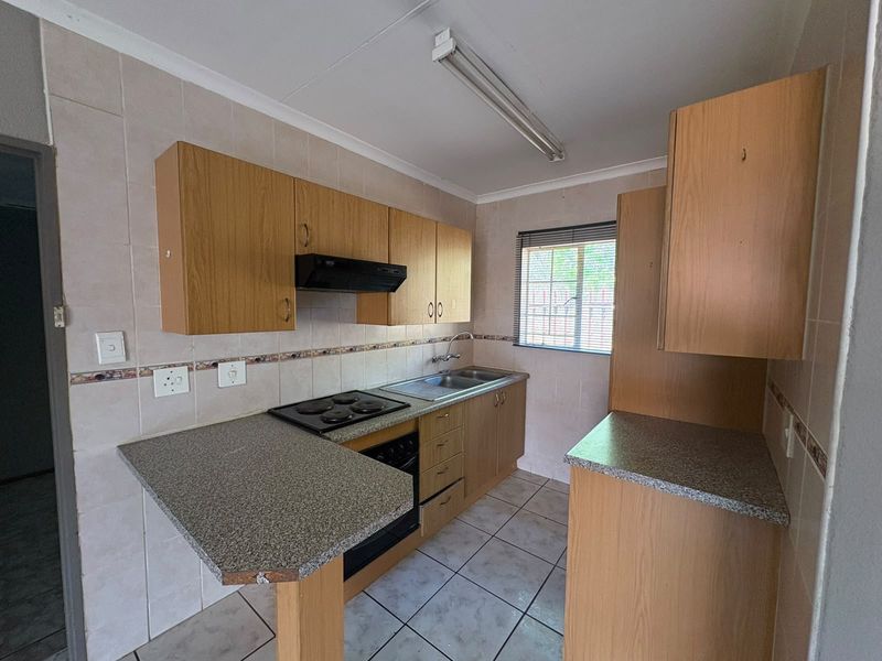 A functional kitchen featuring laminate cabinetry, a built-in electric oven and hob, double sink, and tiled finishes throughout.