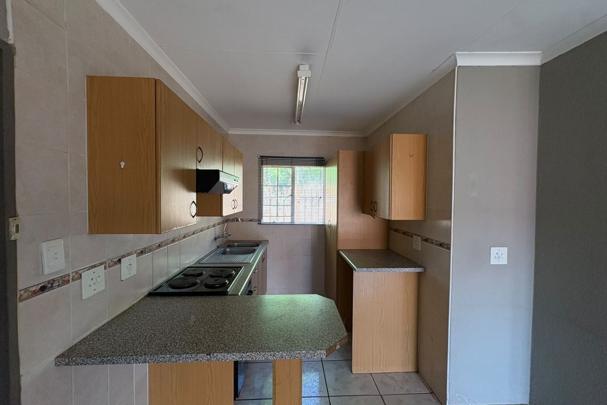 A functional kitchen featuring laminate cabinetry, granite-look countertops, an electric hob, and tiled flooring, offering a clean and practical layout.