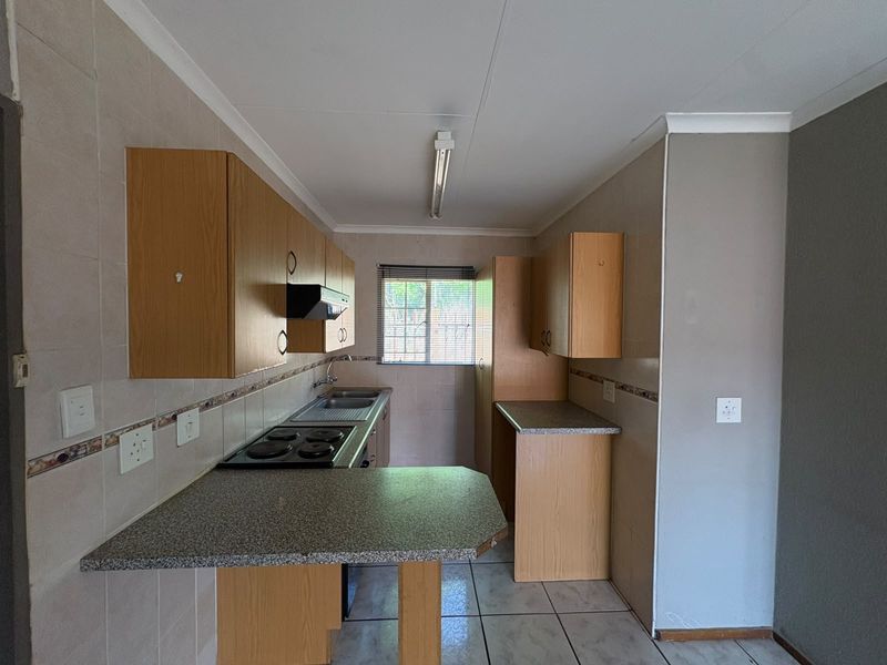 A functional kitchen featuring laminate cabinetry, granite-look countertops, an electric hob, and tiled flooring, offering a clean and practical layout.