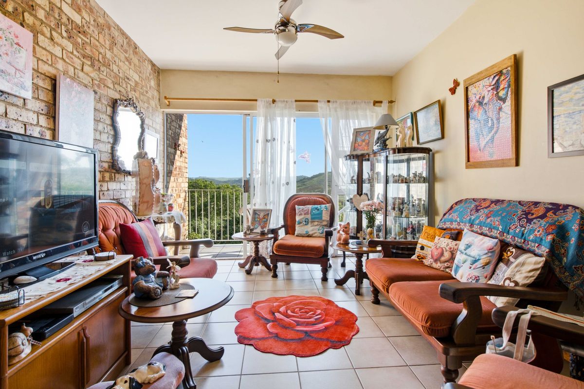 A living room featuring an exposed brick wall, tiled flooring, and a sliding glass door leading to a balcony with scenic views.