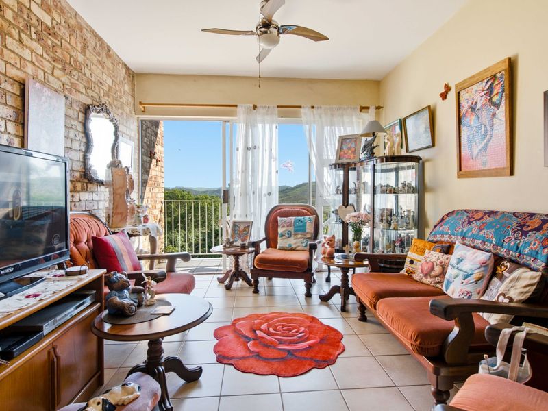 A living room featuring an exposed brick wall, tiled flooring, and a sliding glass door leading to a balcony with scenic views.