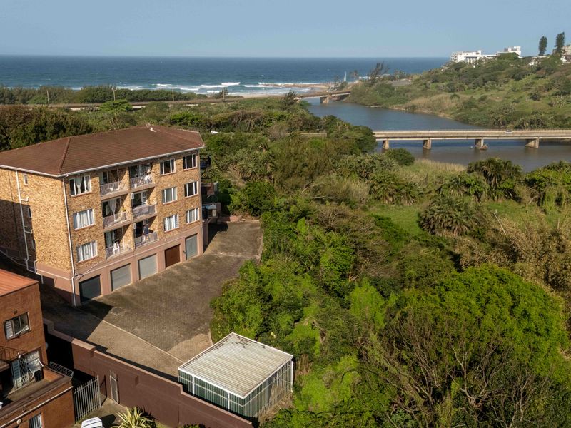 Aerial view of a multi-story townhouse complex featuring paved driveway access, balconies, and proximity to the river and coastline.
