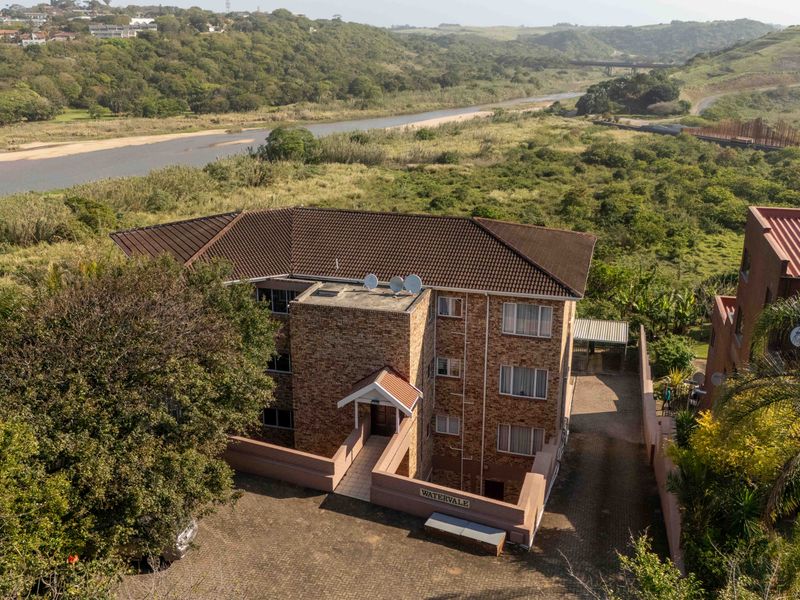 Aerial view of a multi-story brick townhouse complex featuring a tiled roof, paved driveway, and scenic river landscape surroundings.