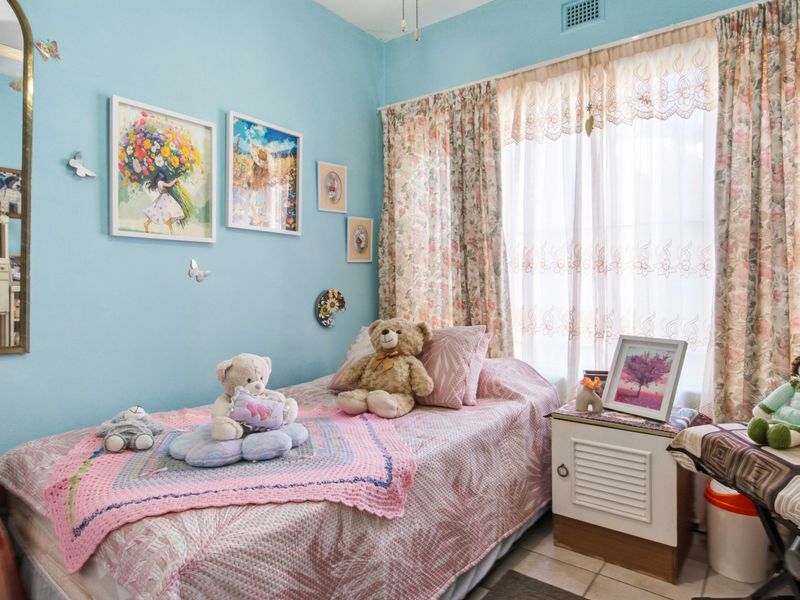 A bedroom featuring light blue walls, tiled flooring, and a ceiling ventilation unit, providing a functional space with natural light.