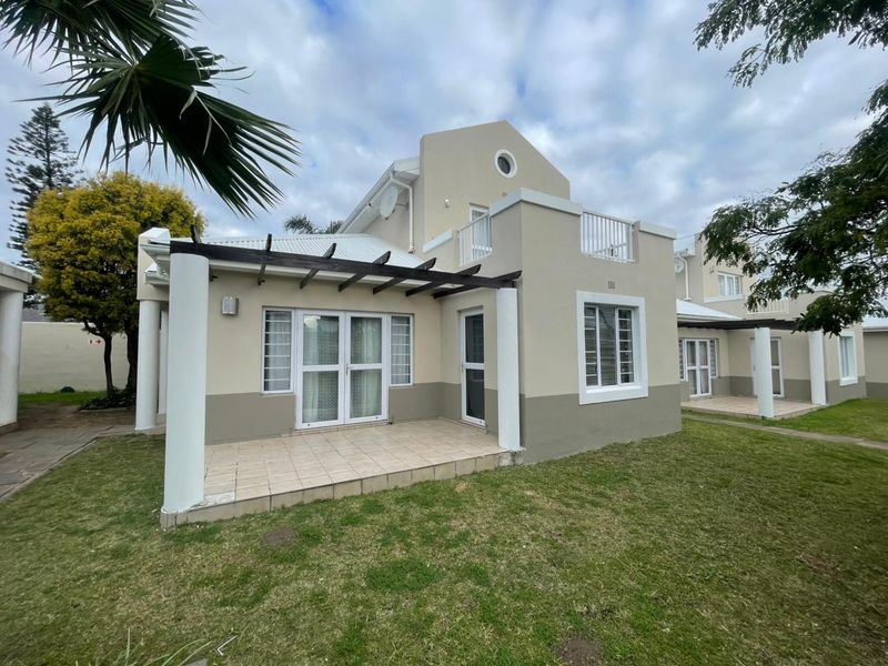 Rear view of the apartment featuring a tiled patio with a timber pergola, upper-level balcony, and well-maintained exterior finishes.