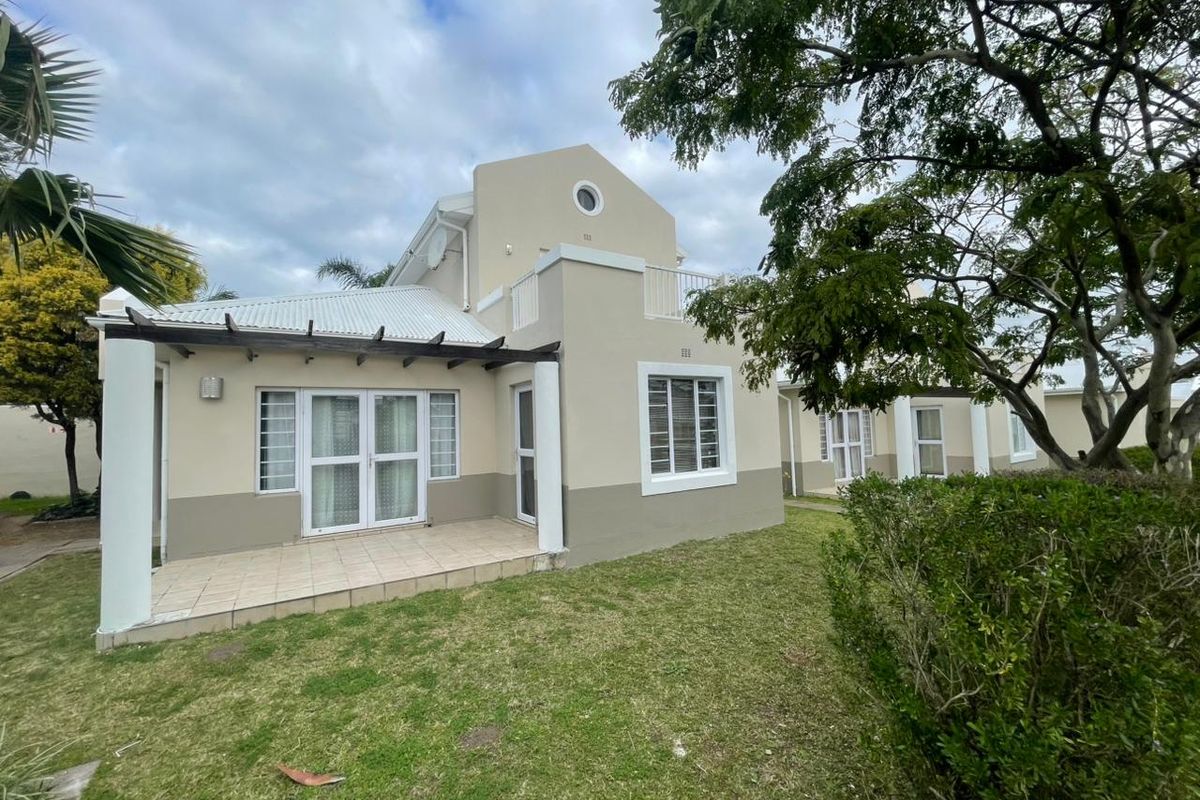 Rear view of the apartment featuring a tiled patio with a timber pergola, a small upper balcony, and access to a private garden area.