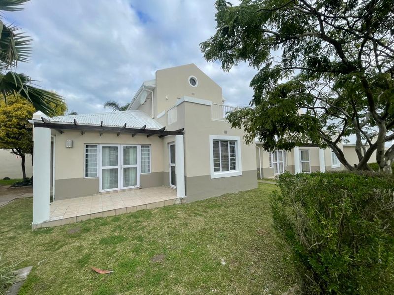 Rear view of the apartment featuring a tiled patio with a timber pergola, a small upper balcony, and access to a private garden area.