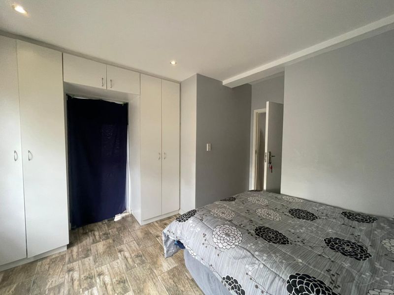 A bedroom featuring built-in cupboards, recessed downlighting, and wood-look tiled flooring.