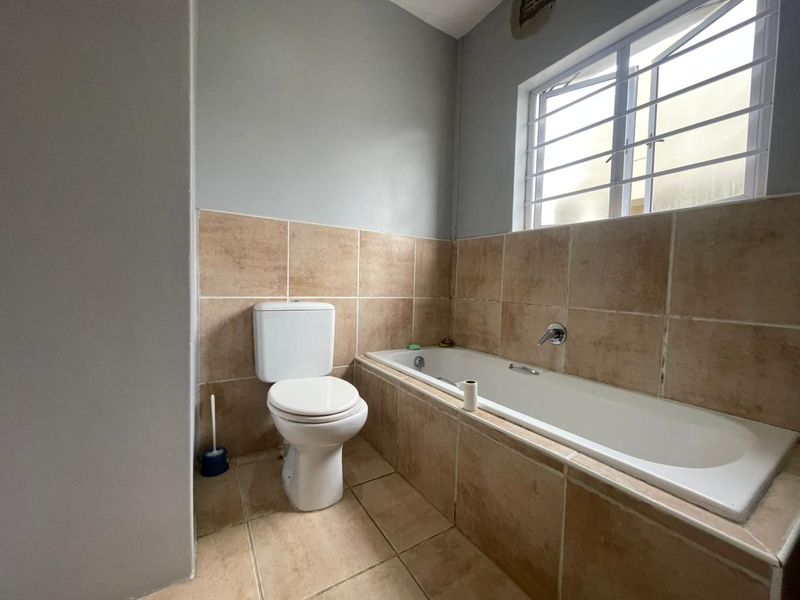 A functional bathroom featuring a built-in bathtub, toilet, and neutral ceramic tiling with a window providing natural light and ventilation.