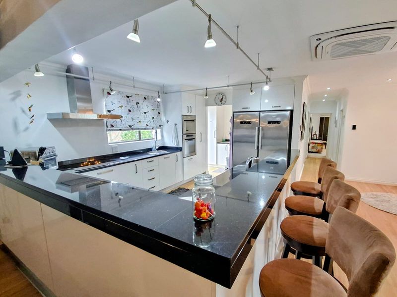 Modern kitchen featuring sleek white cabinetry, dark granite countertops, integrated stainless steel appliances, and a breakfast bar with track lighting.