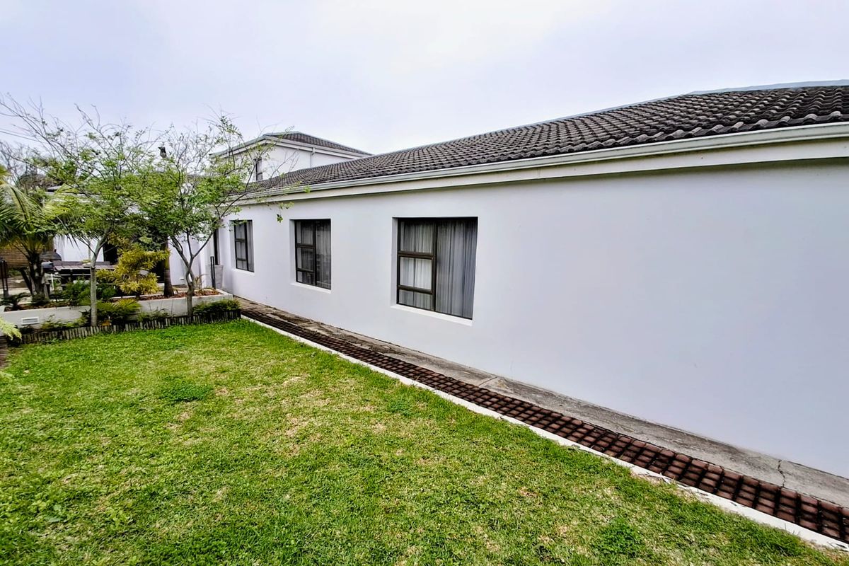 Rear exterior view of the house featuring a tiled roof, white rendered walls, aluminium windows, and a landscaped garden with a paved drainage channel.