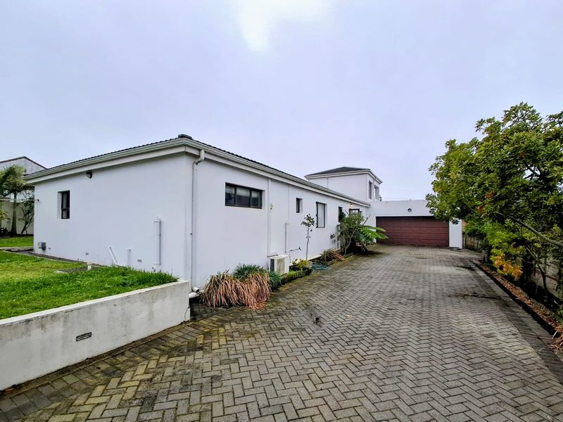 Side view of the property featuring a paved driveway, garage access, and a low retaining wall bordering the lawn area.
