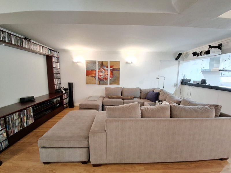 Spacious living room featuring hardwood flooring, a large built-in media shelving unit, and integrated ceiling-mounted projector setup.
