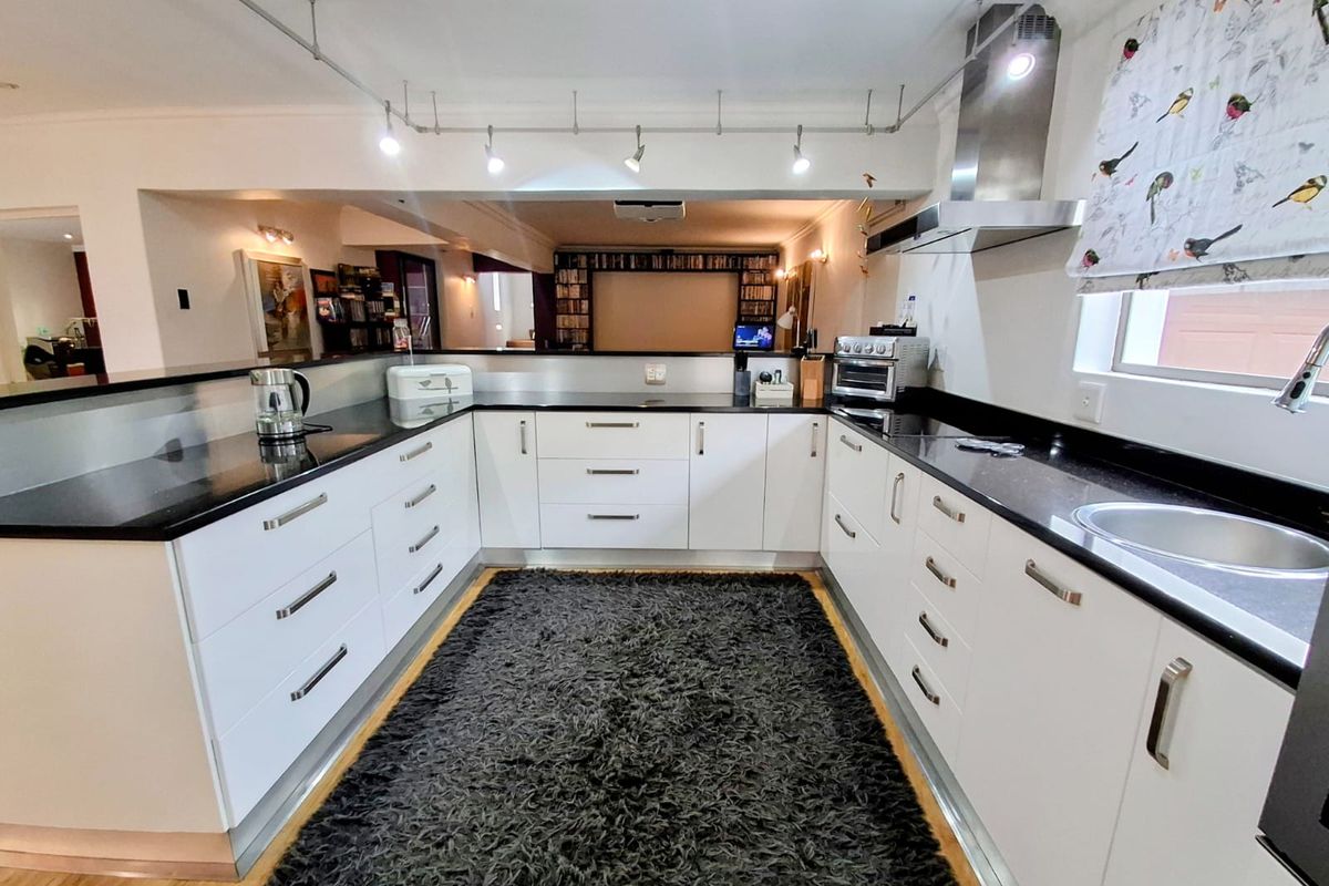Modern U-shaped kitchen featuring white cabinetry, contrasting black granite countertops, stainless steel extractor fan, and integrated track lighting.