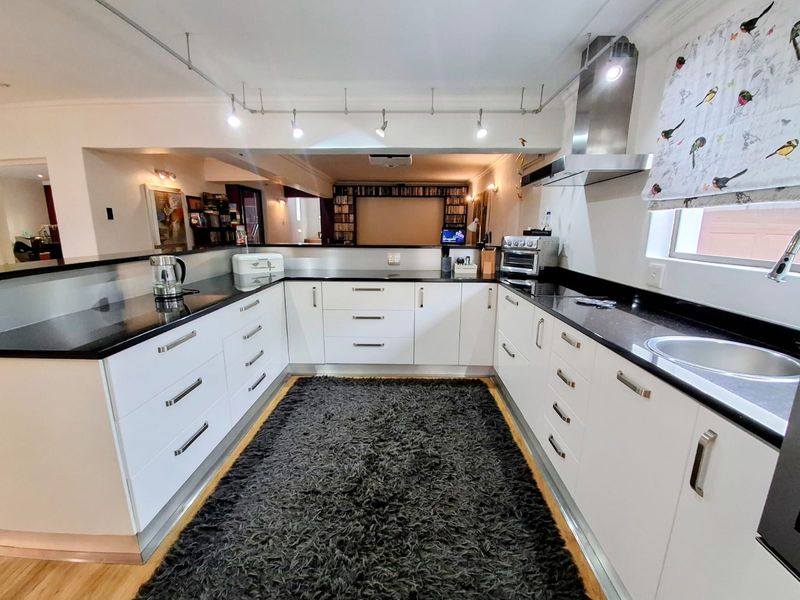 Modern U-shaped kitchen featuring white cabinetry, contrasting black granite countertops, stainless steel extractor fan, and integrated track lighting.