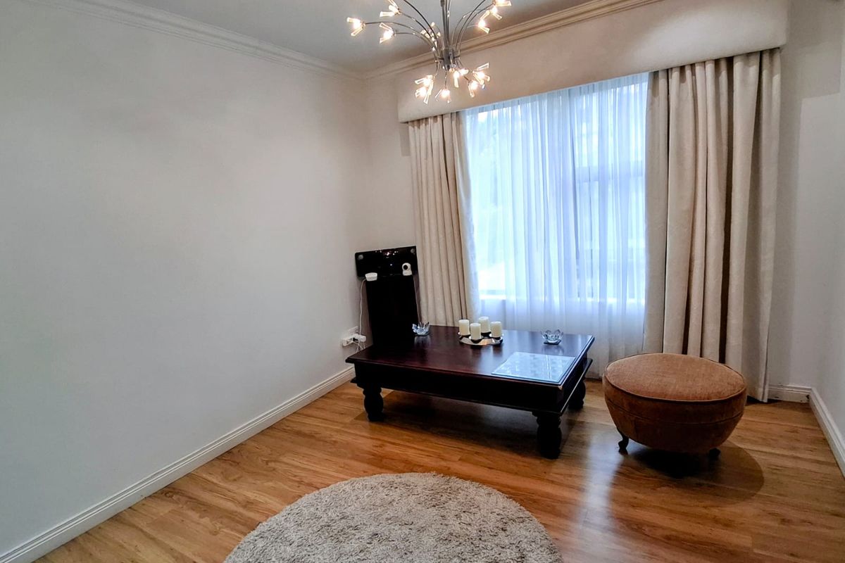 A well-maintained living room featuring hardwood flooring, crown molding, and a decorative light fixture, offering a bright and neutral space.
