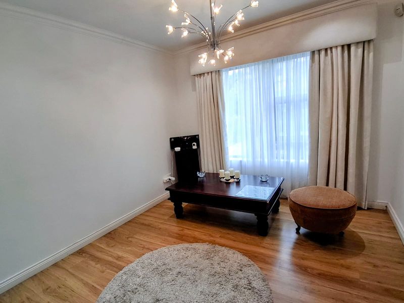 A well-maintained living room featuring hardwood flooring, crown molding, and a decorative light fixture, offering a bright and neutral space.