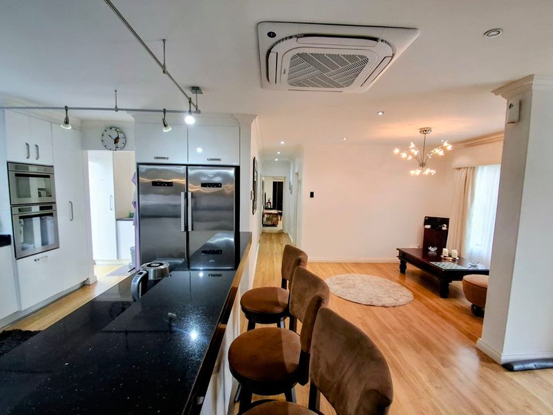 Open-plan living and kitchen area featuring modern cabinetry, granite countertops, built-in appliances, and ceiling-mounted air conditioning with warm hardwood flooring throughout.