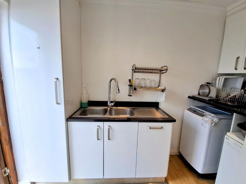 A functional laundry area featuring a double bowl stainless steel sink, gooseneck faucet, laminate countertop, and built-in white cabinetry.