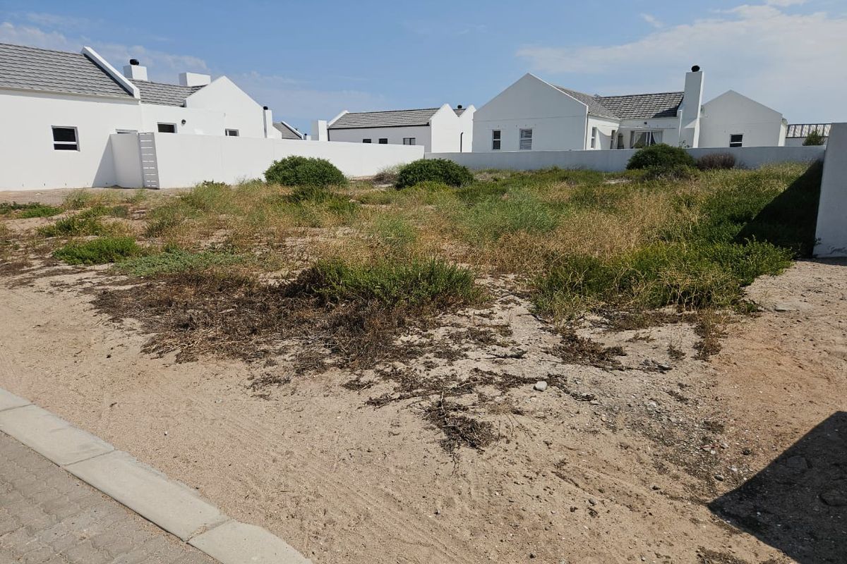 A vacant residential plot featuring sandy ground, natural vegetation, and surrounding boundary walls in a developed neighborhood.