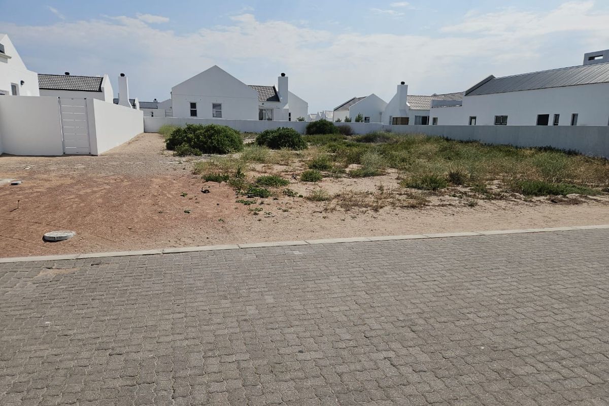 A vacant residential plot featuring a paved street frontage and established boundary walls in a developed estate setting.