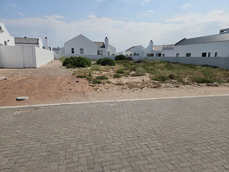 A vacant residential plot featuring a paved street frontage and established boundary walls in a developed estate setting.