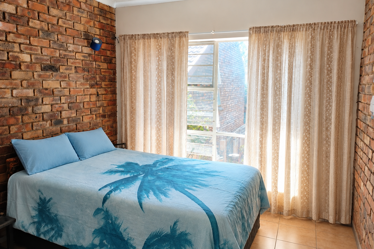 A bedroom featuring exposed brick feature walls, tiled flooring, and a large window allowing natural light.