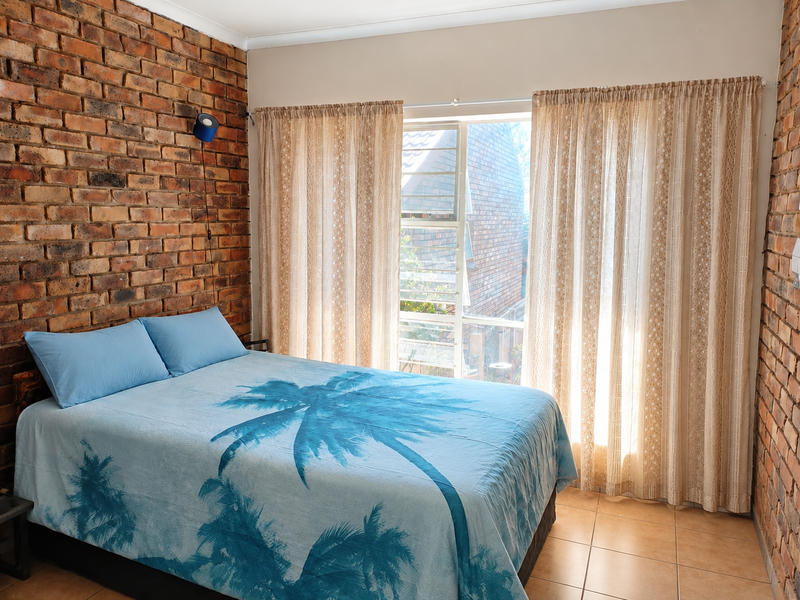 A bedroom featuring exposed brick feature walls, tiled flooring, and a large window allowing natural light.