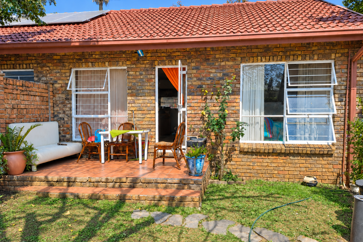 Rear view of a face brick apartment featuring a tiled patio, solar panels, and casement windows with security bars.