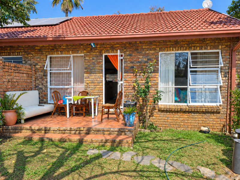 Rear view of a face brick apartment featuring a tiled patio, solar panels, and casement windows with security bars.