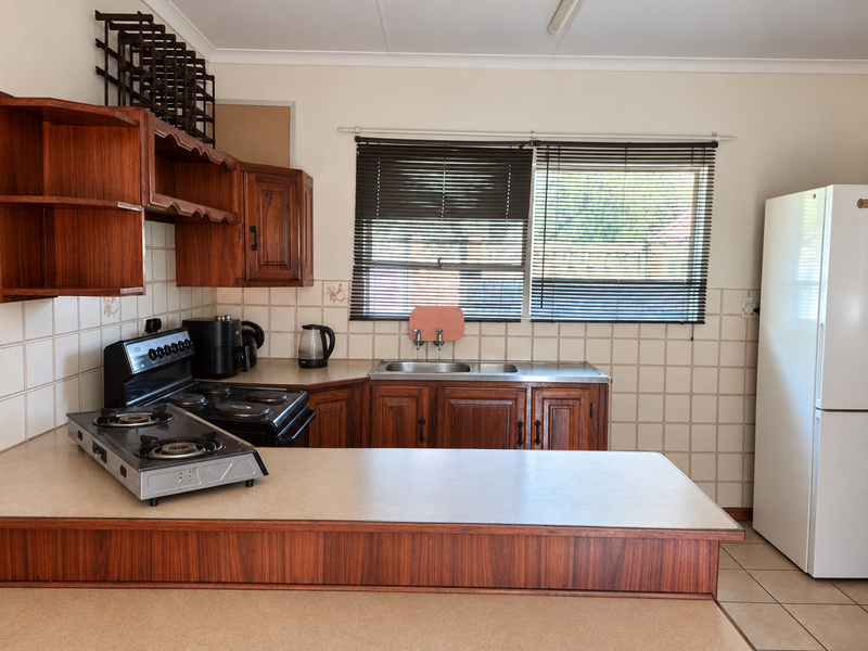 A functional kitchen featuring traditional wooden cabinetry, laminate countertops, a double bowl sink, and tiled backsplash with neutral ceramic flooring.
