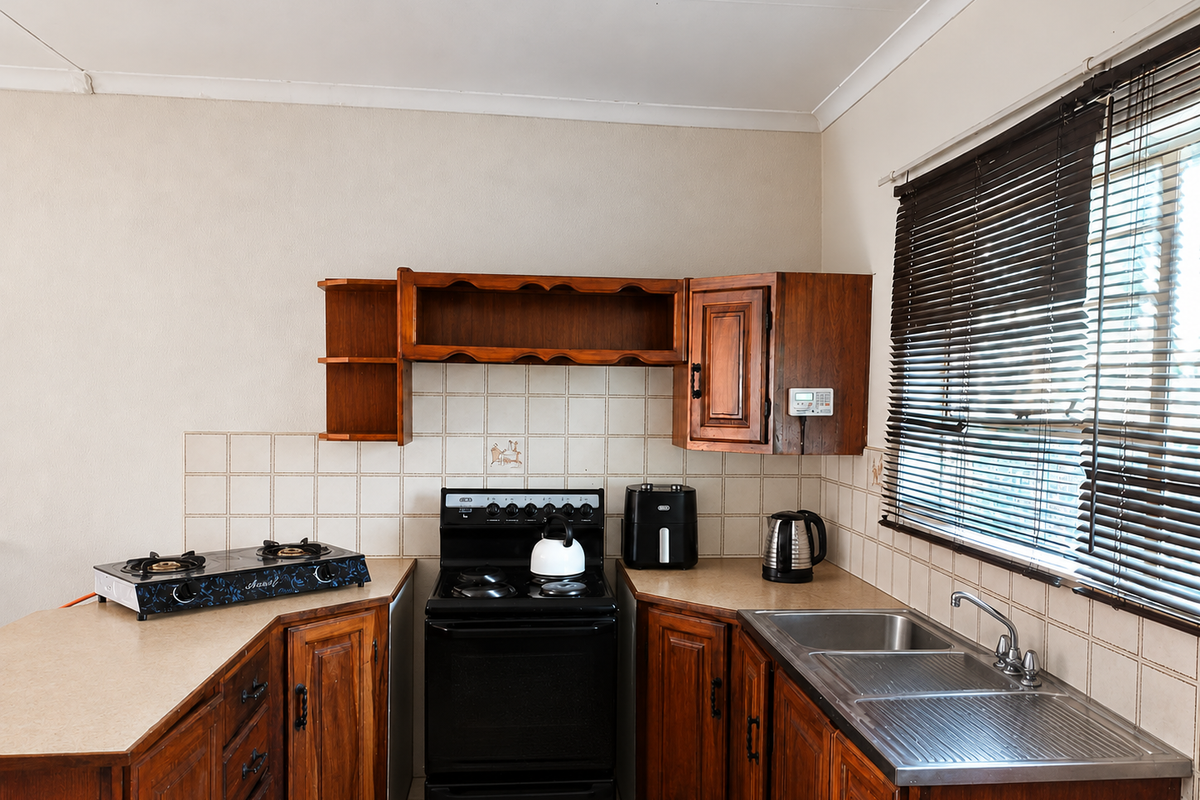 A functional kitchen featuring traditional wooden cabinetry, laminate countertops, a stainless steel sink, and a tiled backsplash with a freestanding stove.