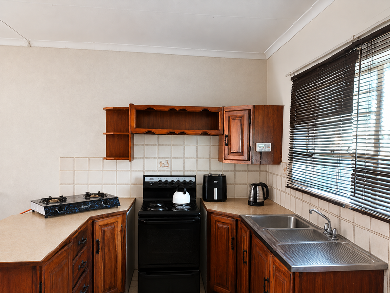 A functional kitchen featuring traditional wooden cabinetry, laminate countertops, a stainless steel sink, and a tiled backsplash with a freestanding stove.