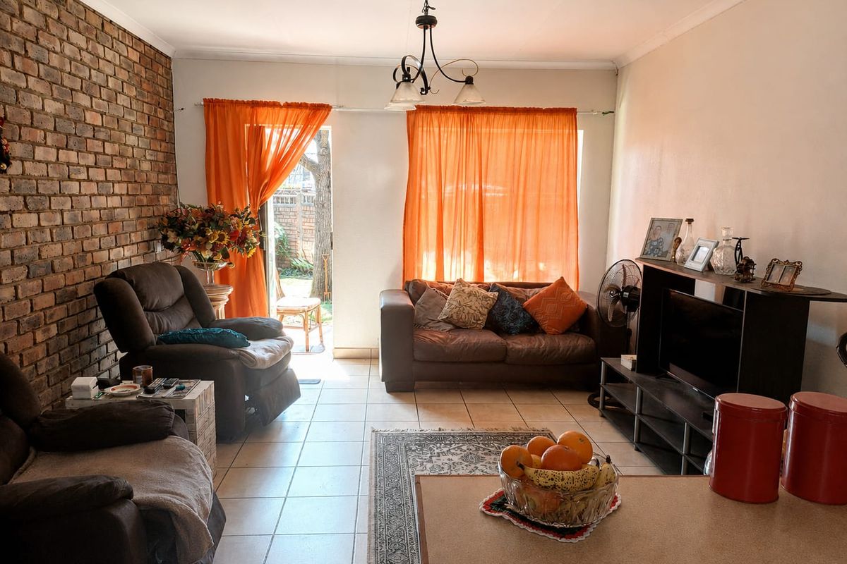 A living room featuring an exposed brick feature wall, tiled flooring, and a sliding glass door providing access to the outdoor area.