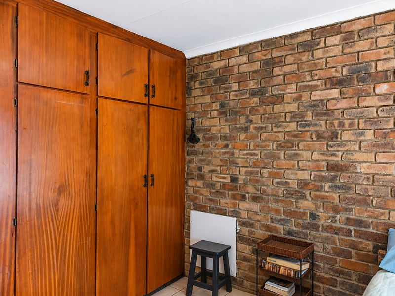 Bedroom featuring a prominent exposed brick wall and extensive built-in wooden cabinetry providing ample storage space.