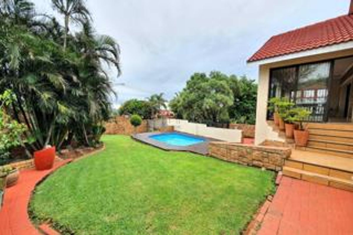 Rear garden area featuring a swimming pool, stone retaining wall, and a tiled patio leading to the main dwelling via sliding glass doors.